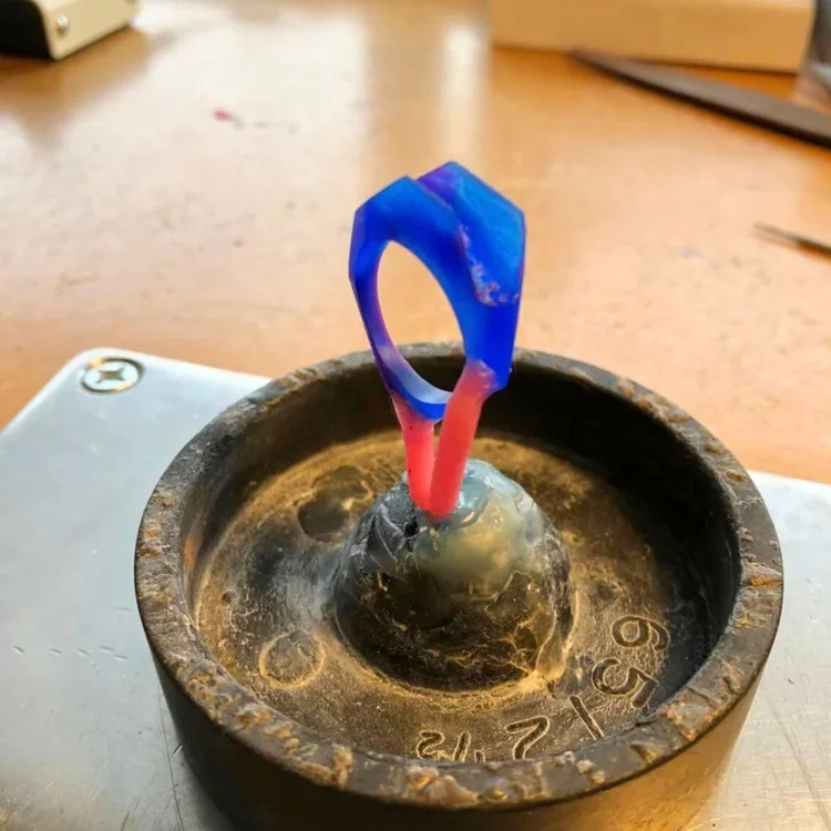 A blue and red wax ring form standing in a dark casting bowl on the bench