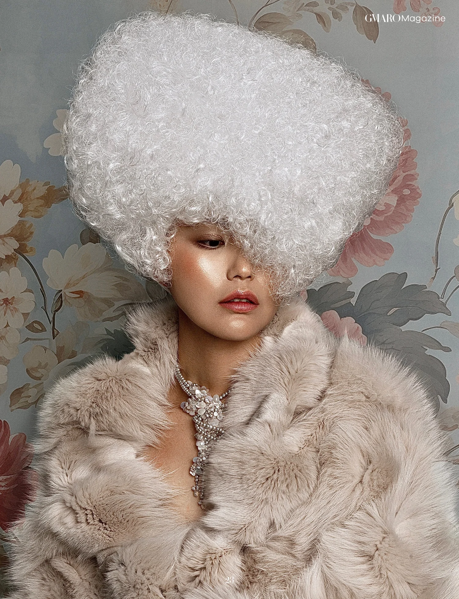 GMARO Magazine page: a model in a cream fur coat and white headpiece against a floral wall, wearing a pearl necklace by Andrea Li