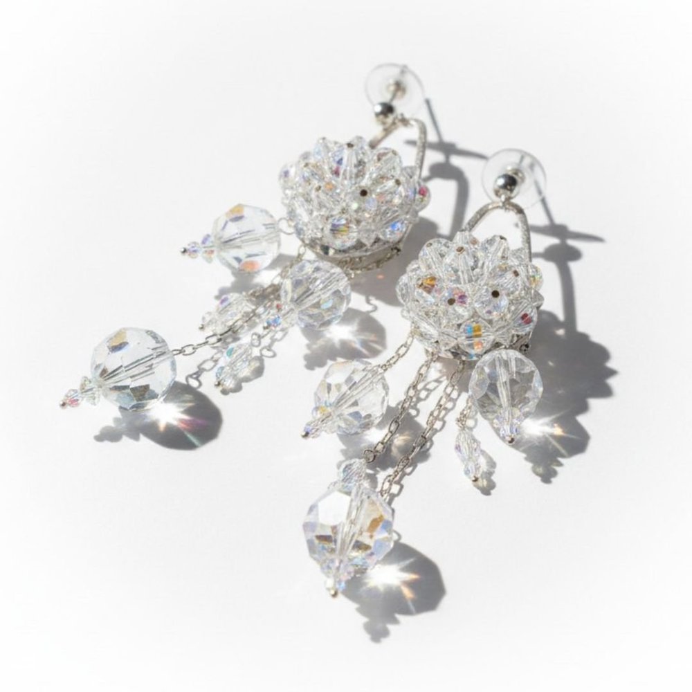 Close-up of vintage crystal earrings with faceted clear beads and dangling drops casting bright shadows on white.