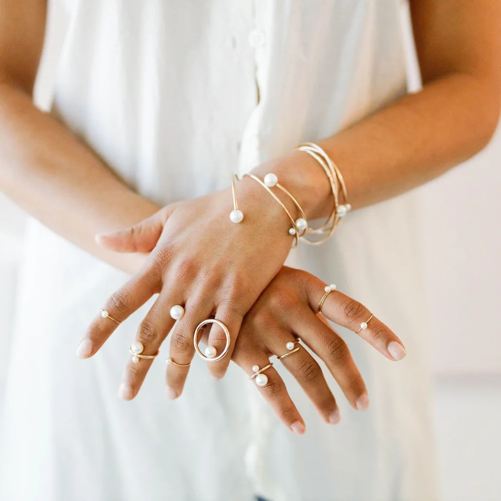 Crossed hands wearing several Andrea Li gold and pearl rings and bangles, by Andrea Li