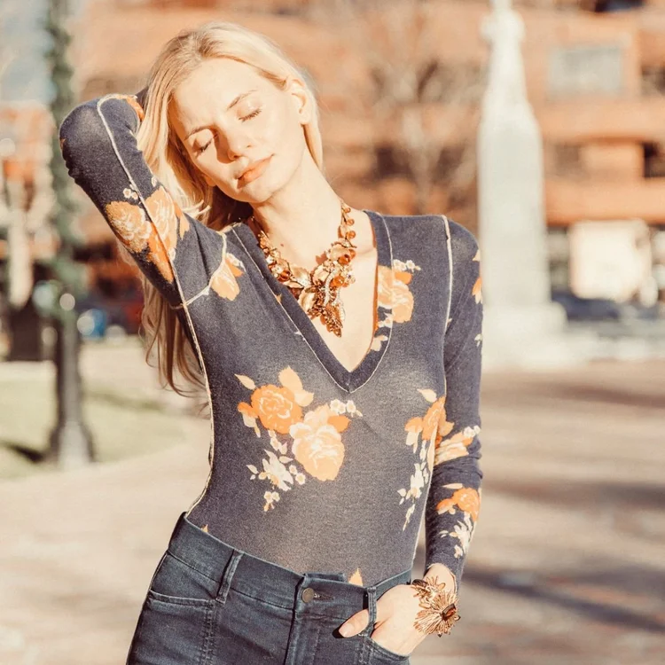 Model with eyes closed in a floral print top, wearing a vintage statement necklace