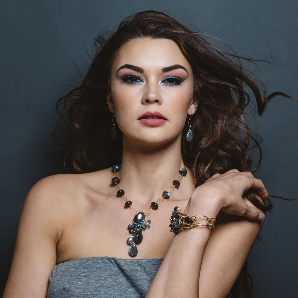 A model in a gray strapless top wearing an Andrea Li gemstone statement necklace and a gemstone cuff