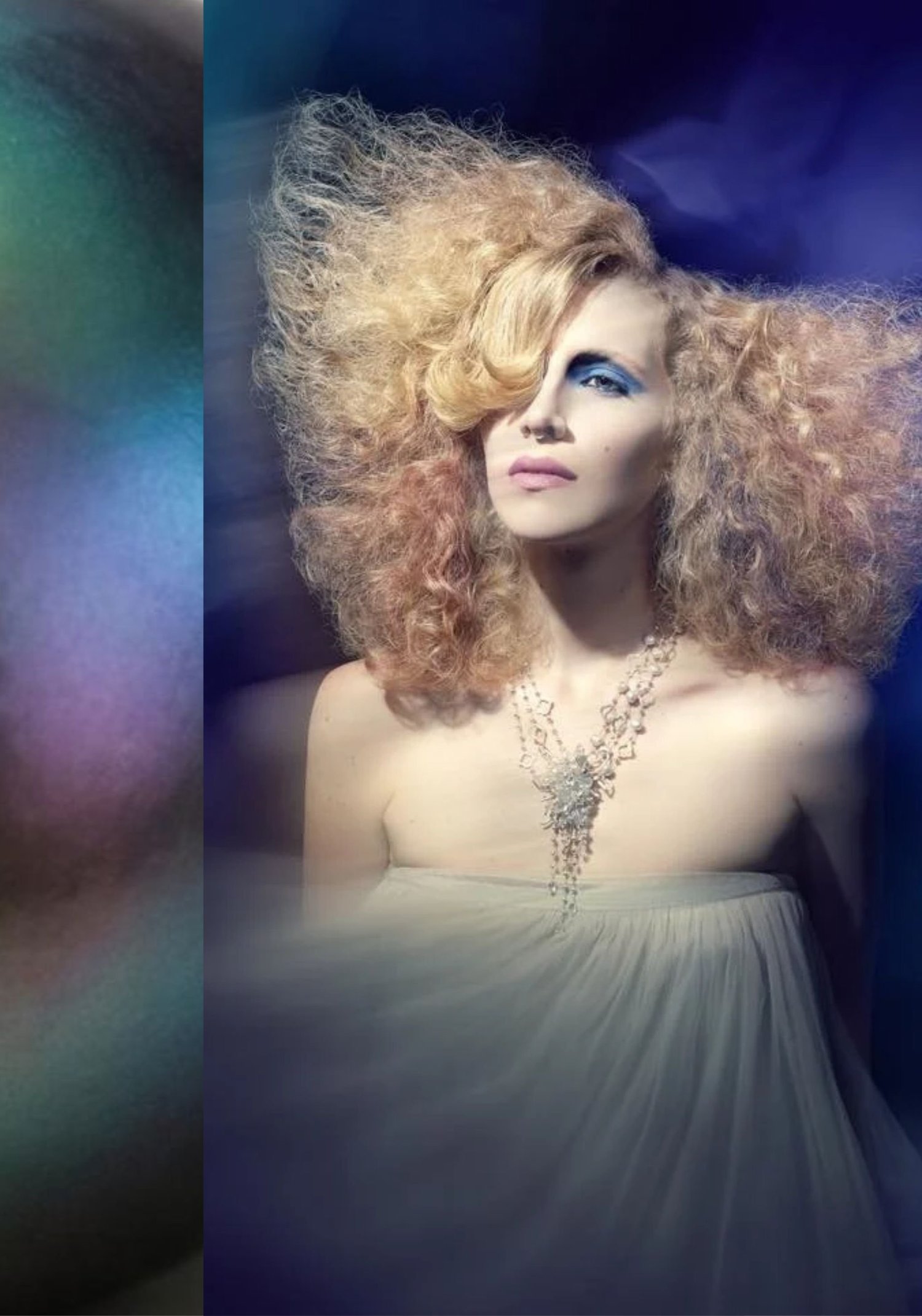 A model with voluminous strawberry-blonde curls in a strapless ivory gown, wearing a multi-strand white necklace with a cascading cluster at the center