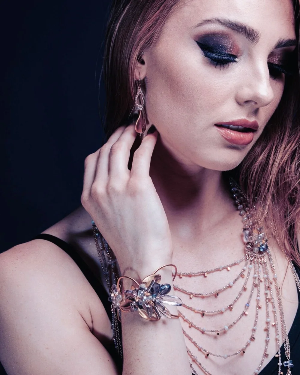 A model touching her ear, wearing an Andrea Li moonstone cluster bracelet and a layered chain necklace, by Andrea Li