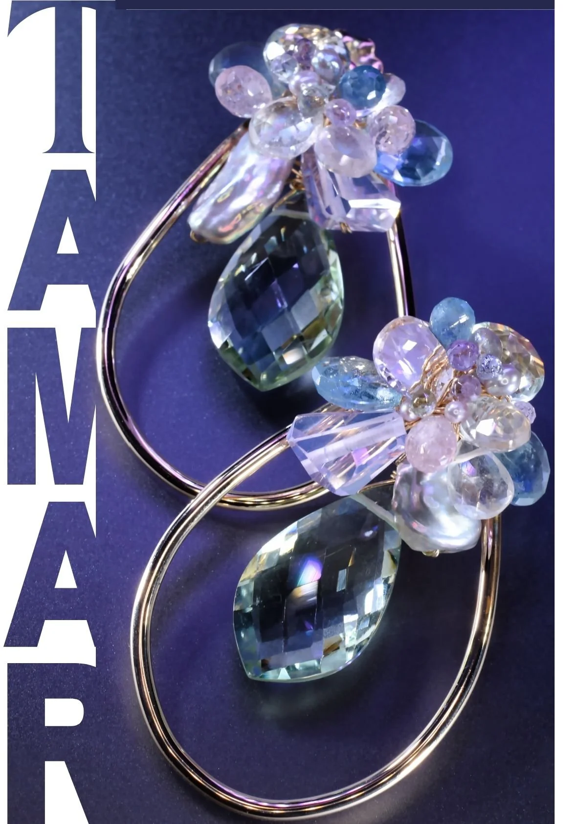 Close-up of TAMAR pastel gemstone drop earrings featuring elongated gold hoops, clustered pink and blue stones with pearl accents, and large faceted blue-green gemstone drops on a deep violet background.