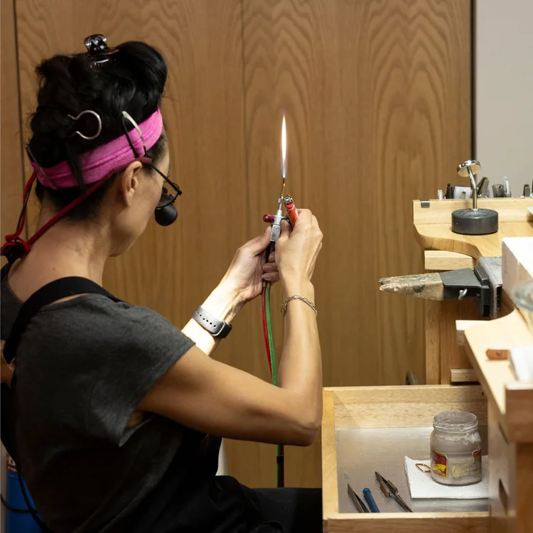 Andrea Li in loupes lighting a small torch at her bench