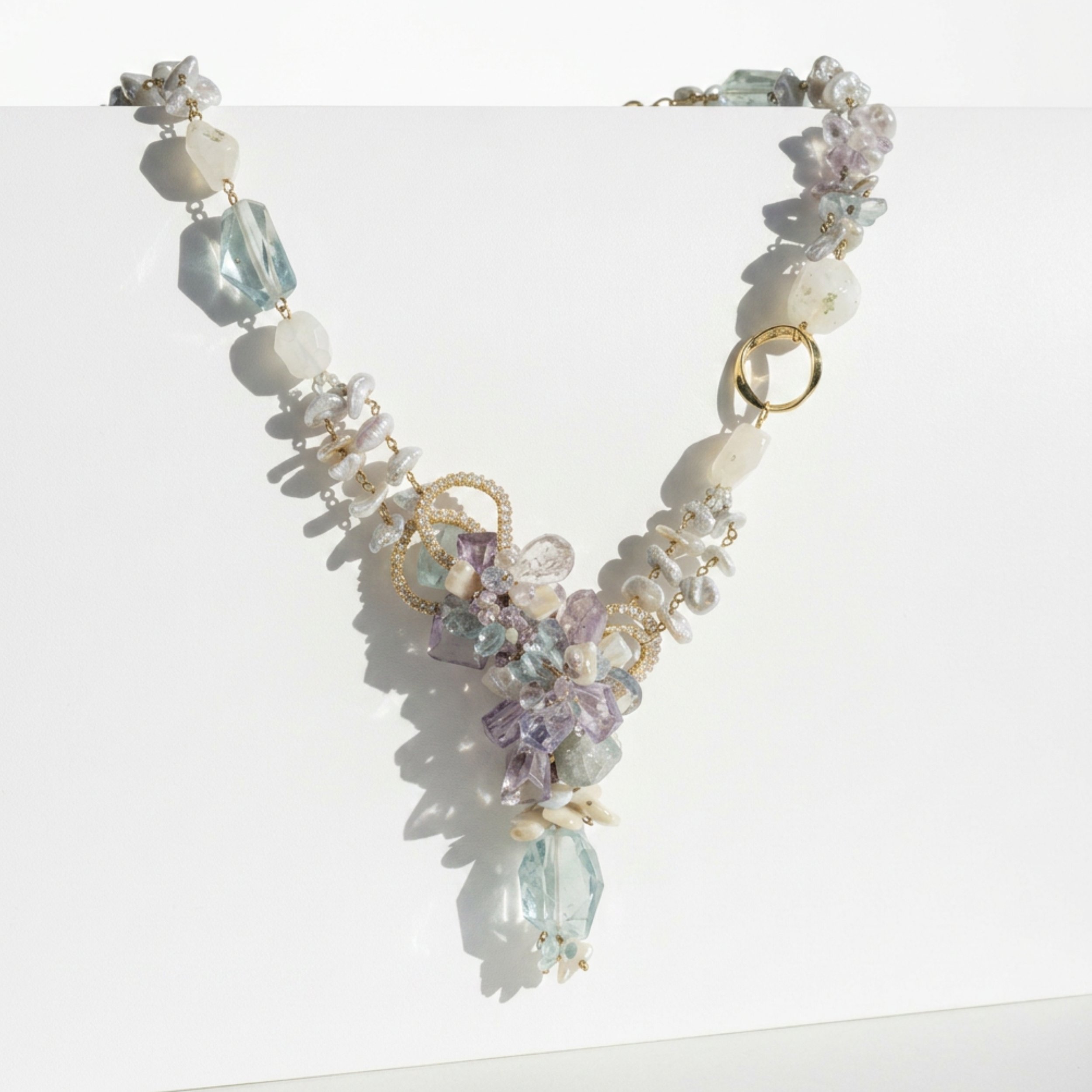 Pastel gemstone statement necklace draped on a white display, featuring aquamarine, moonstone, amethyst, and gold details.