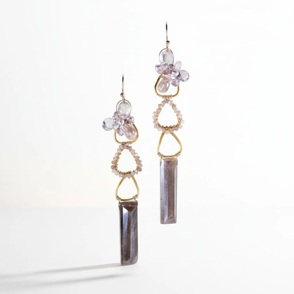 Pair of delicate mixed-metal drop earrings with pale lavender gemstones and long rectangular crystal pendants, casting soft shadows.