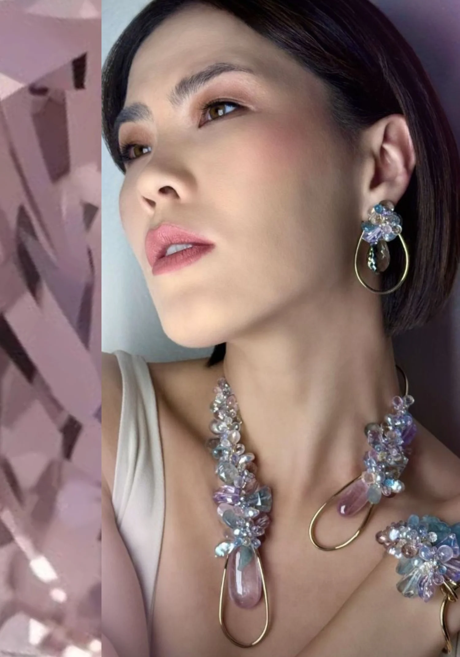 A model wearing gold teardrop earrings, a necklace and a cuff, all clustered with pale blue and pink gemstones