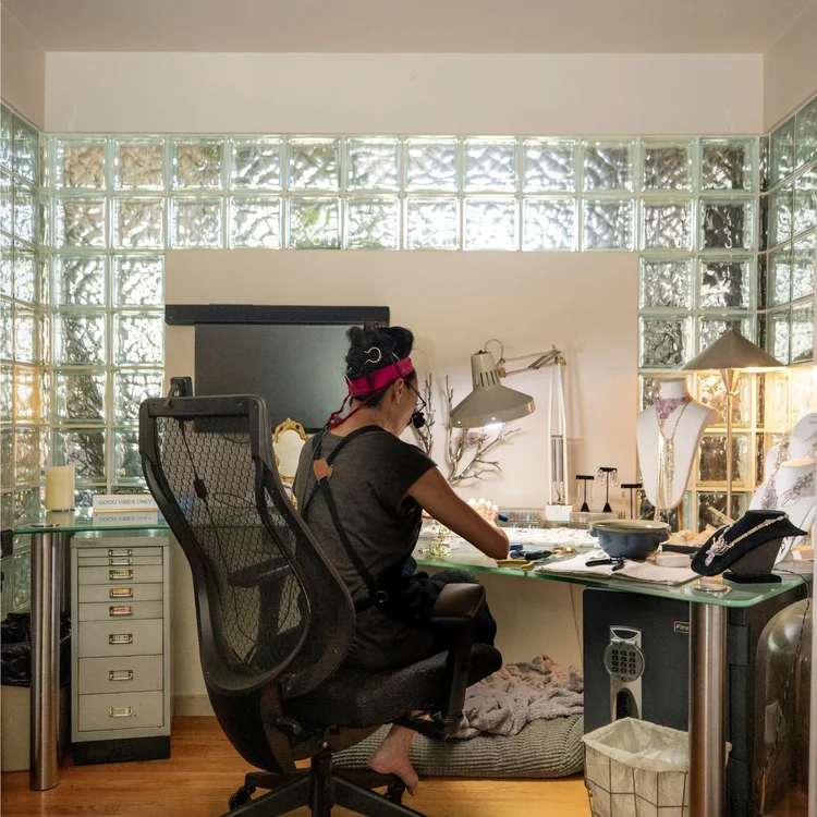Andrea Li working at a glass-topped desk in her studio, lit by a wall of glass blocks