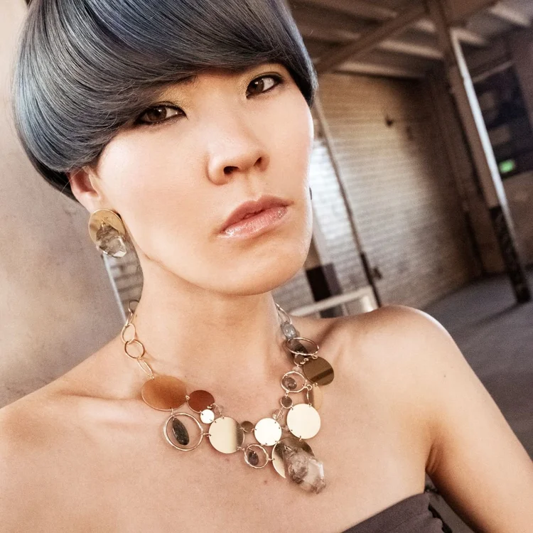 A model with a sleek gray bob in a strapless top wearing a gold disk and crystal statement necklace
