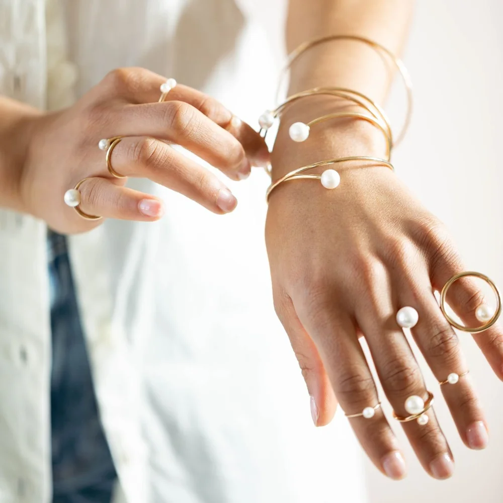 Hands wearing Andrea Li gold and pearl open rings and pearl bangles, by Andrea Li