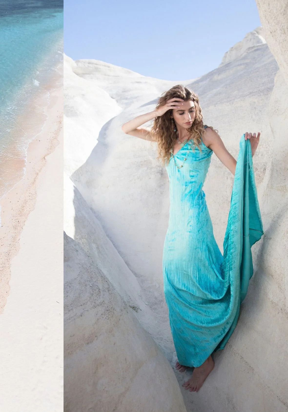 A model in a flowing turquoise dress among white rock formations, beside a strip of turquoise sea and white sand.