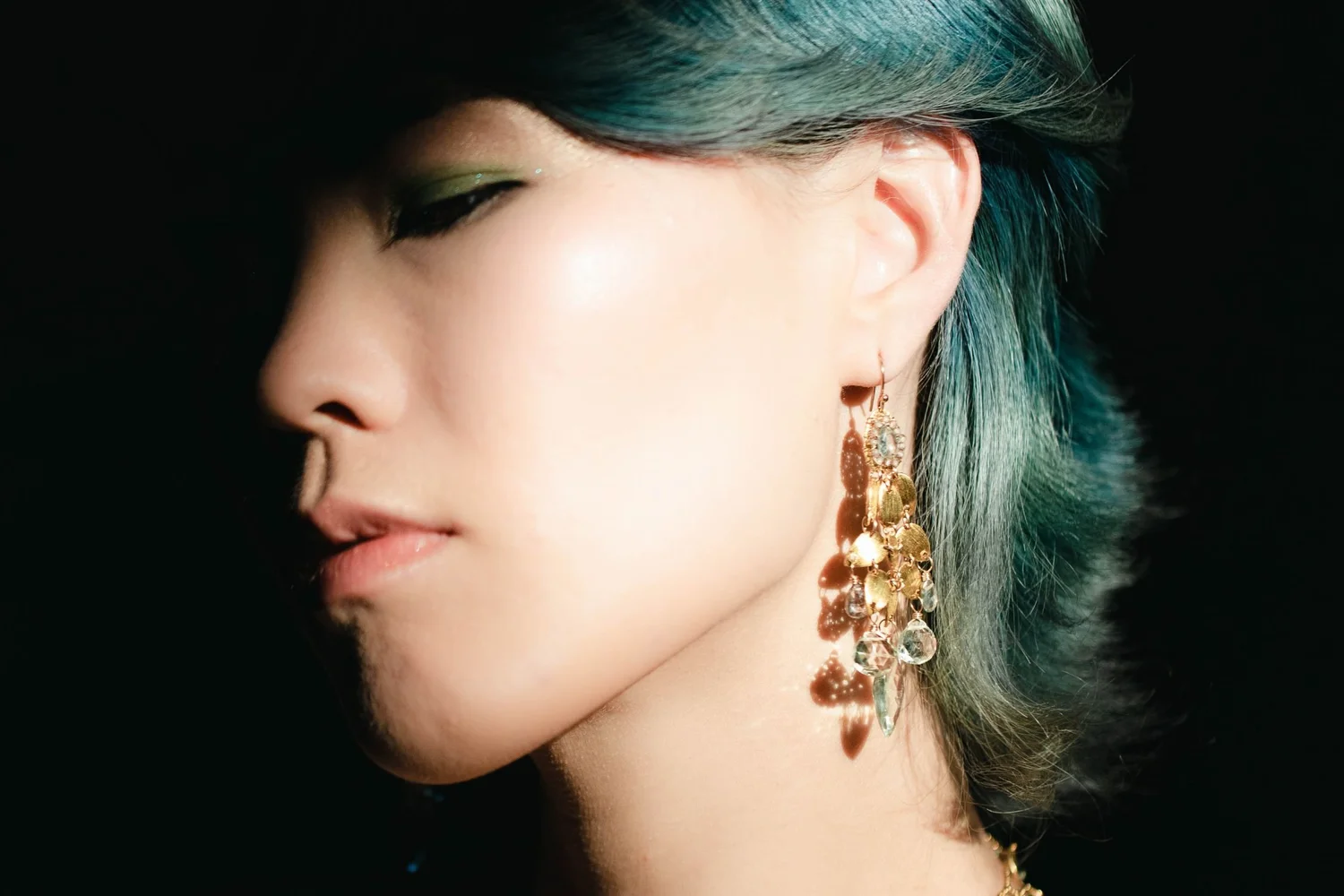 Profile of a model with teal hair against a dark background, wearing an Andrea Li gold cluster drop earring, by Andrea Li