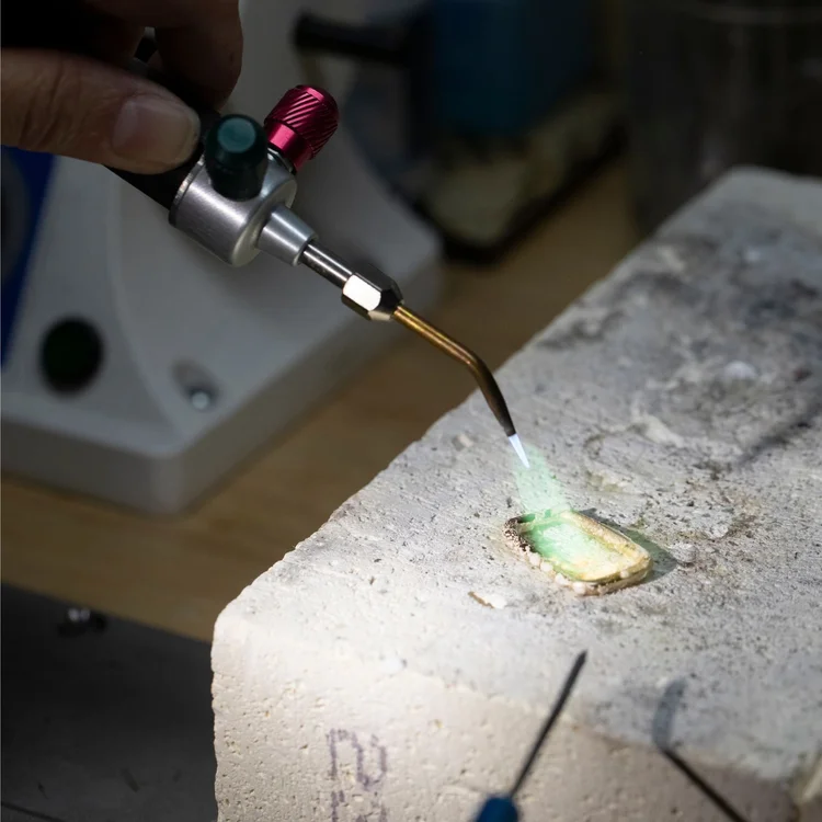 A torch flame soldering a gold frame on a soldering block