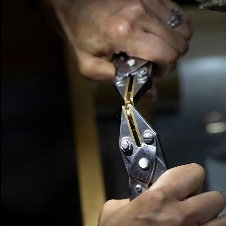 Hands gripping a gold piece in a pair of parallel pliers
