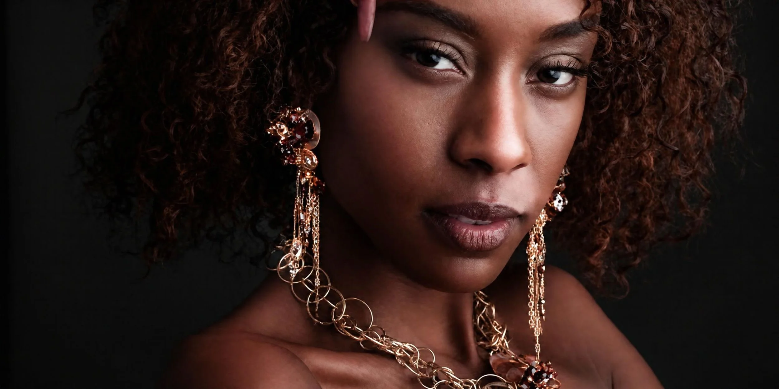 A model with dark curls wearing long Andrea Li gold gemstone earrings and layered necklaces, by Andrea Li