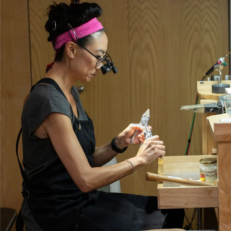 Andrea Li at her bench in loupes, studying a silver piece in her hands
