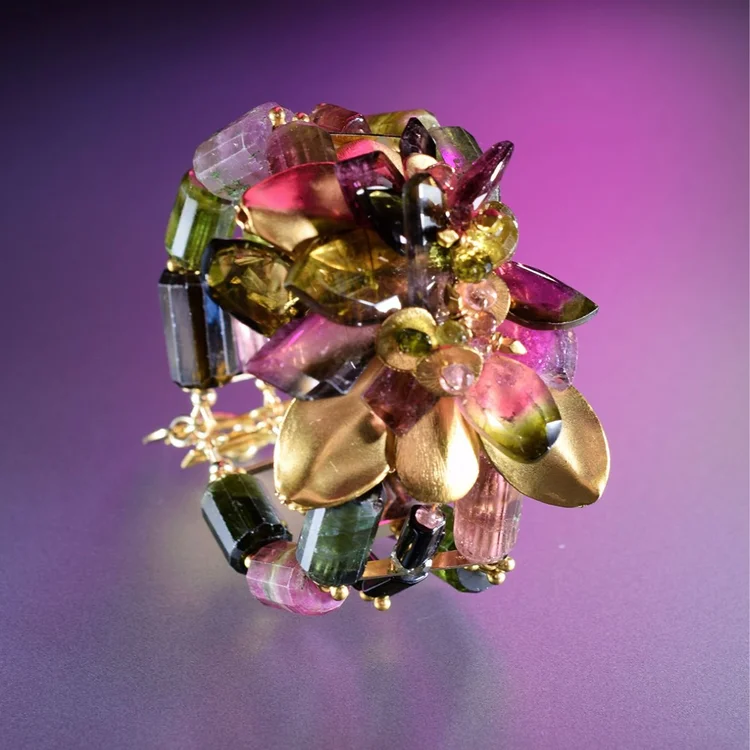 A statement ring of pink, green and gold gemstones against a violet background