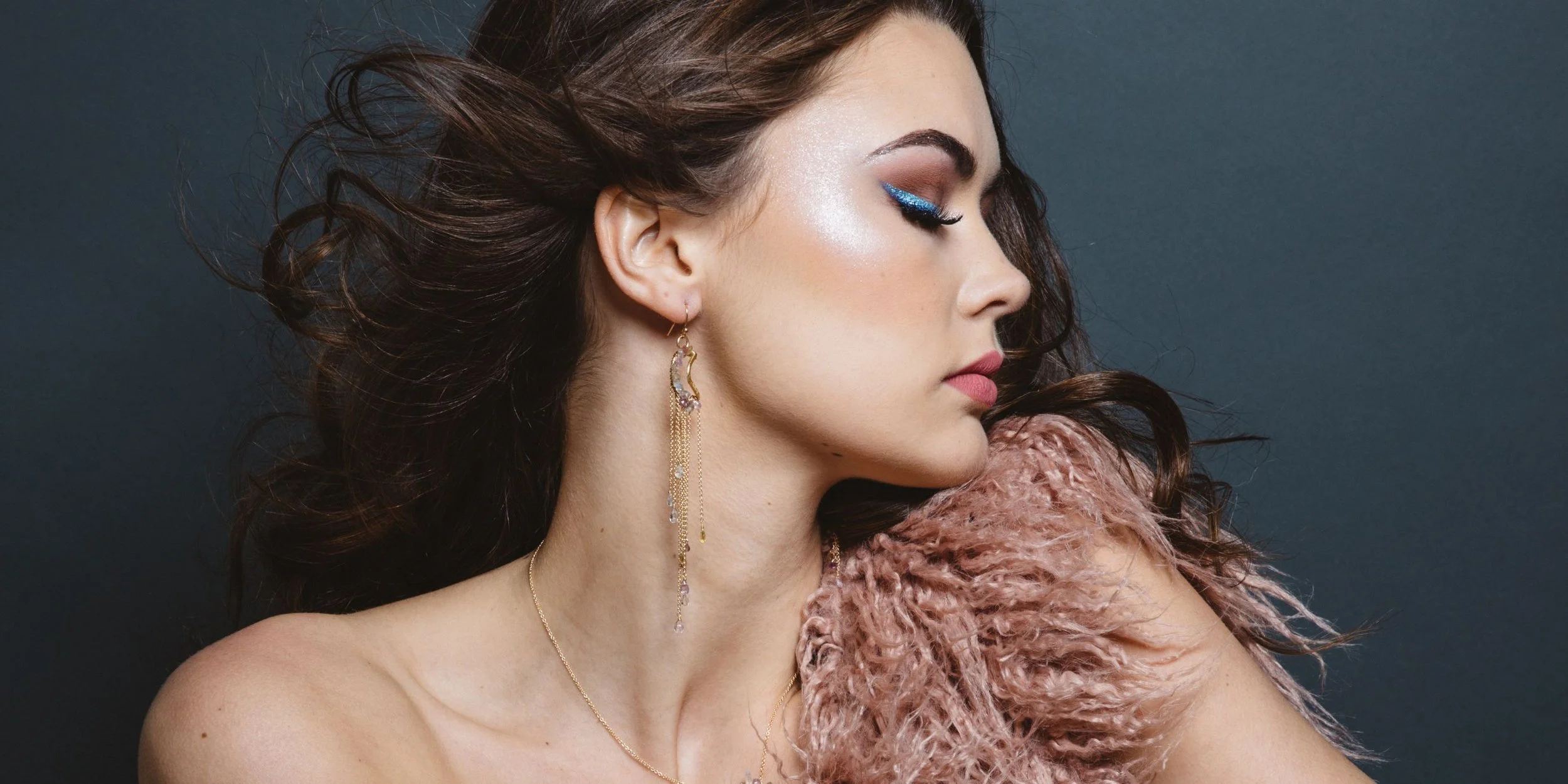 A model in a blush feather wrap turning her head, wearing long Andrea Li sapphire drop earrings, by Andrea Li