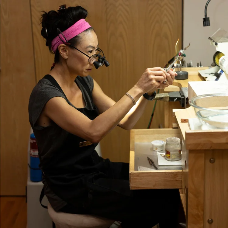 Andrea Li at her bench in loupes, filing a piece in her hands