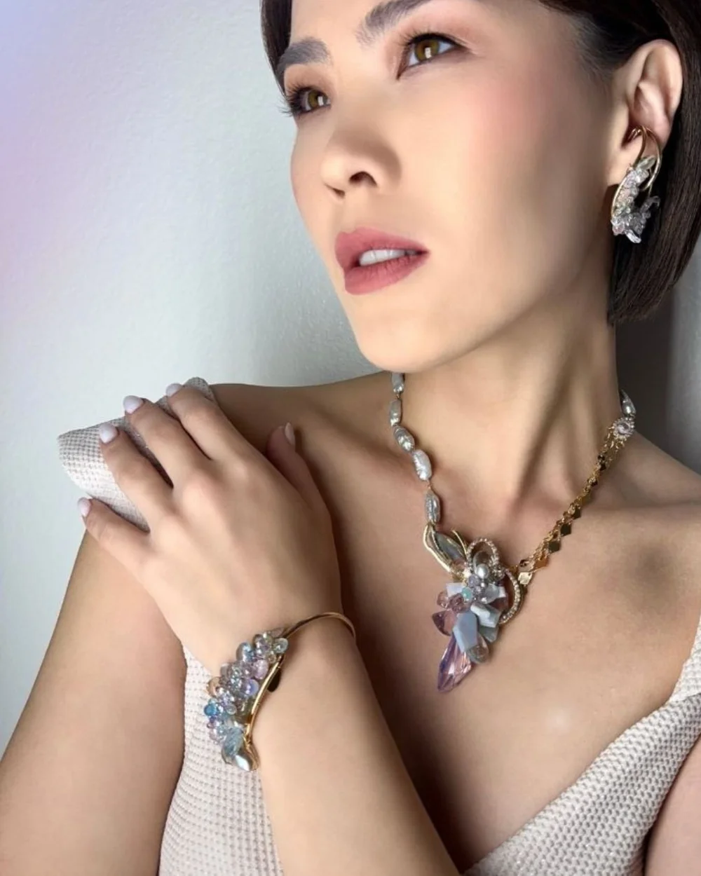A model with her hand at her shoulder, wearing an Andrea Li pastel gemstone cuff and gemstone necklace, by Andrea Li