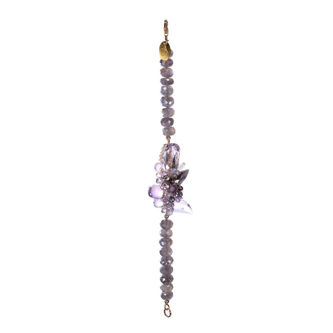 Delicate bracelet with faceted lavender beads and a central floral cluster of purple gemstones and pearls, finished with gold-toned clasps and links on a light gray background.