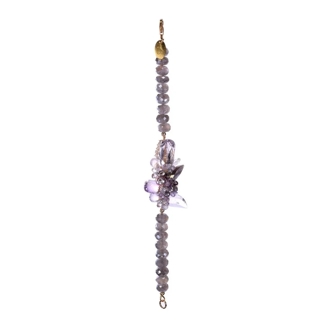 Delicate bracelet with faceted lavender beads and a central floral cluster of purple gemstones and pearls, finished with gold-toned clasps and links on a light gray background.