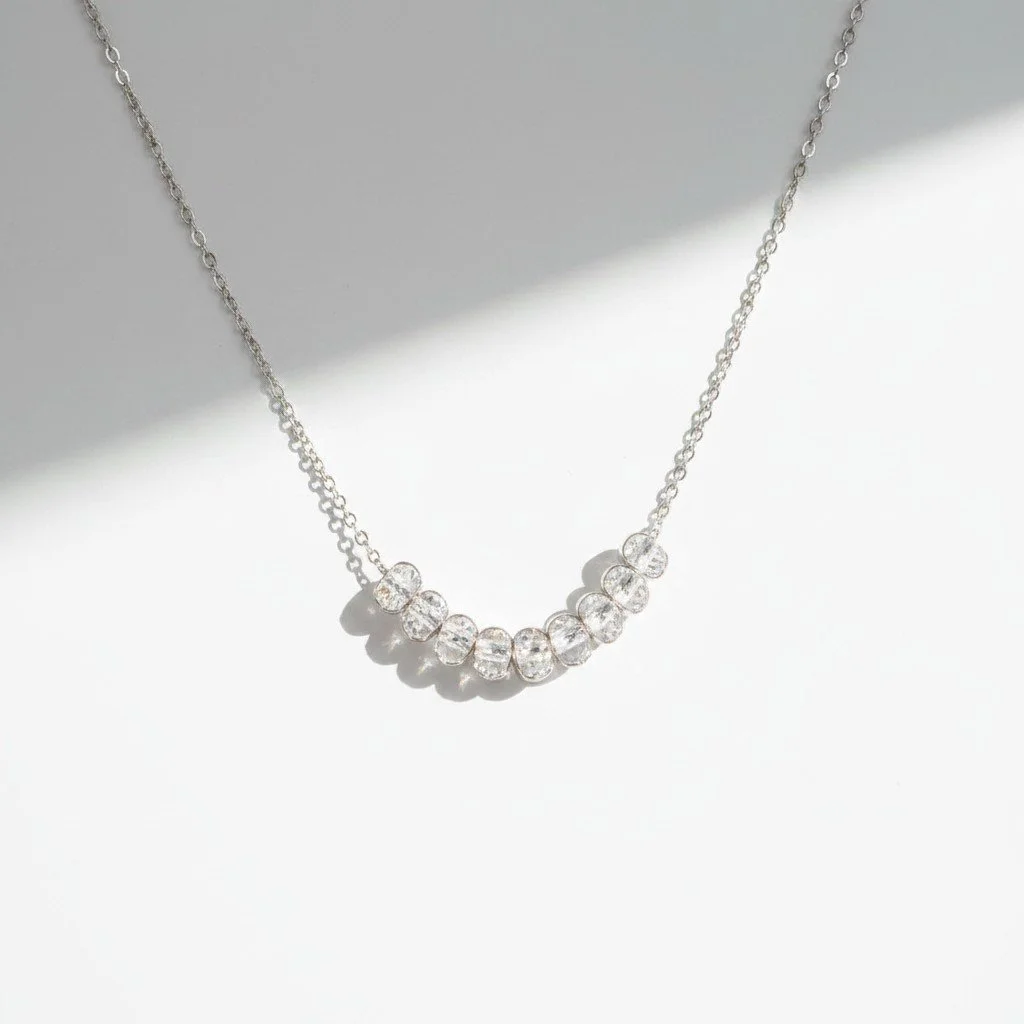 Delicate silver necklace with a curved row of clear white topaz beads on a fine chain, photographed on a soft white background.