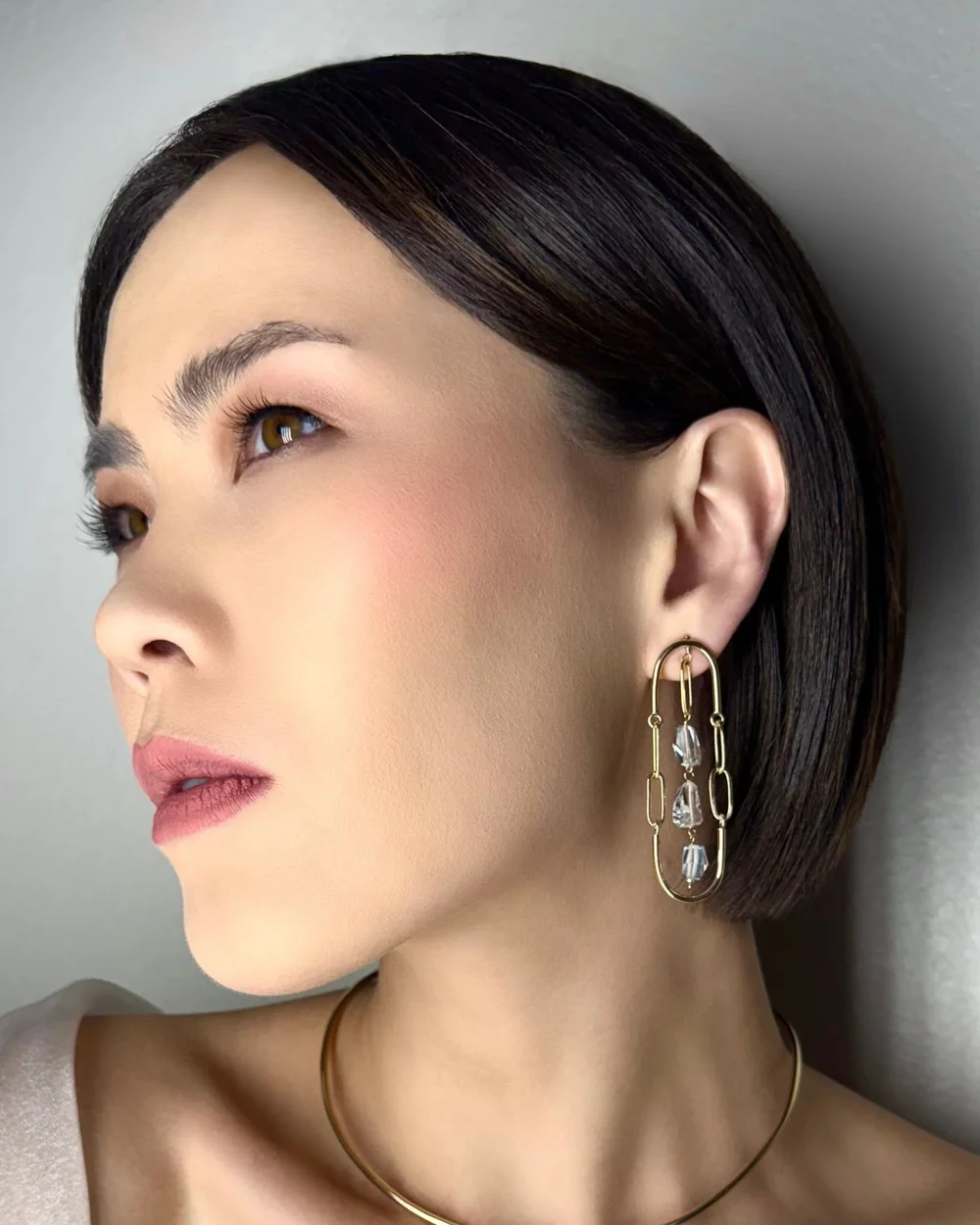 A model with a dark bob wearing Andrea Li gold chain-link drop earrings set with pale gemstones, by Andrea Li