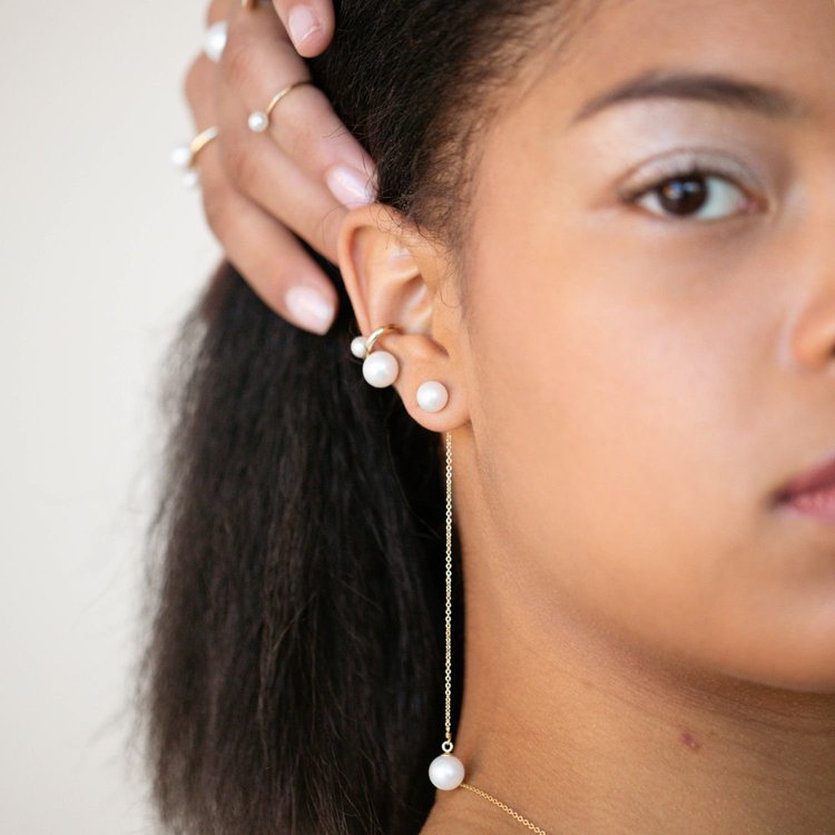 A model touching her ear, wearing an Andrea Li pearl ear climber with a long pearl chain drop, by Andrea Li