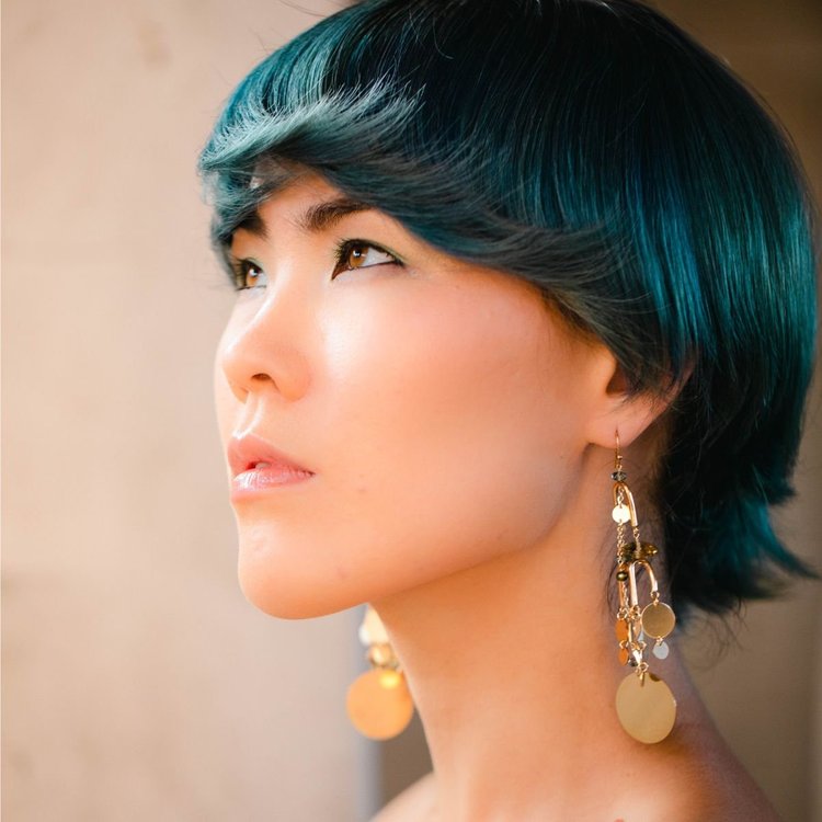 A model with teal hair in profile wearing long gold disk drop earrings