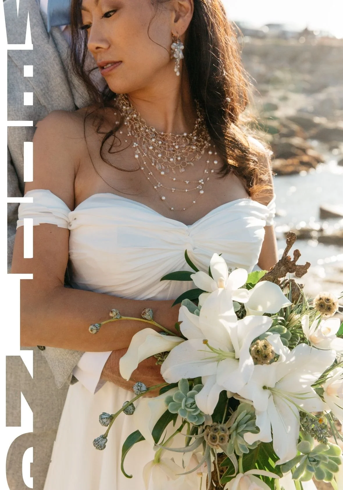 Close-up portrait of a bride in an off-the-shoulder white gown wearing layered pearl wedding jewelry and drop earrings, holding a bouquet of white lilies and succulents outdoors by the water.