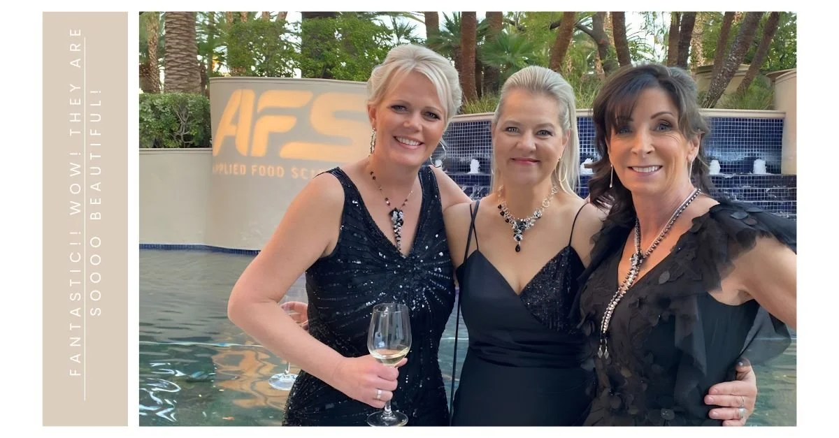 Three women in black evening dresses pose by a fountain at an outdoor event, wearing statement necklaces, with vertical praise text beside them.