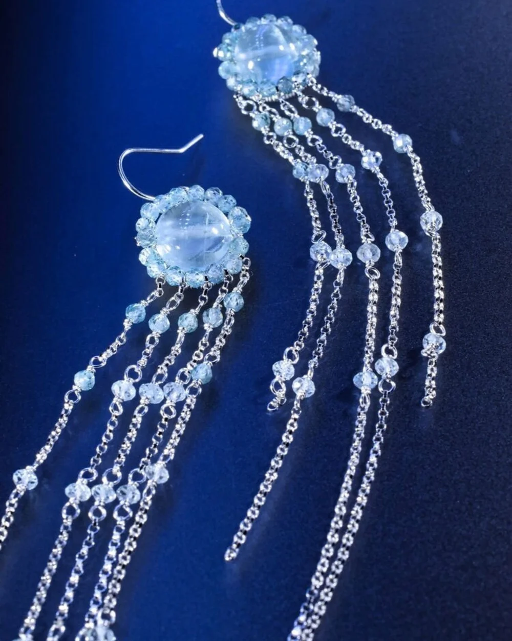 Andrea Li silver earrings with a round pale blue gemstone and long gemstone chains on deep blue, by Andrea Li