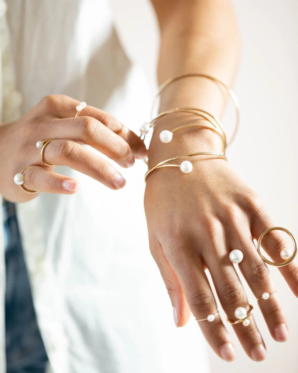 Close view of hands wearing stacked Andrea Li gold and pearl open bangles and pearl rings, by Andrea Li
