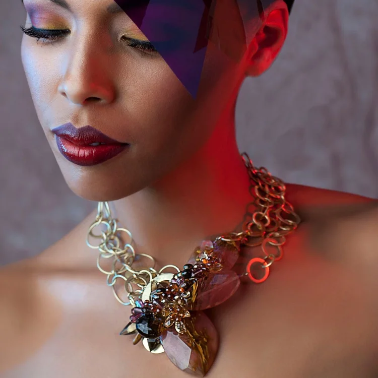 A model with violet makeup wearing a gold chain statement necklace set with dark gemstones