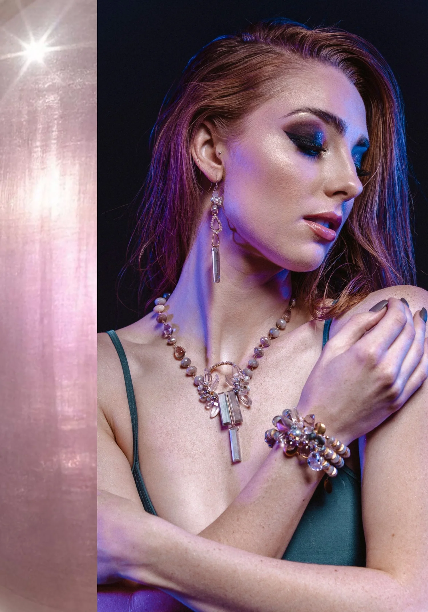 A model with auburn hair wearing long drop earrings, a beaded necklace with a clustered pendant and a clustered bracelet, in pale peach and clear stones