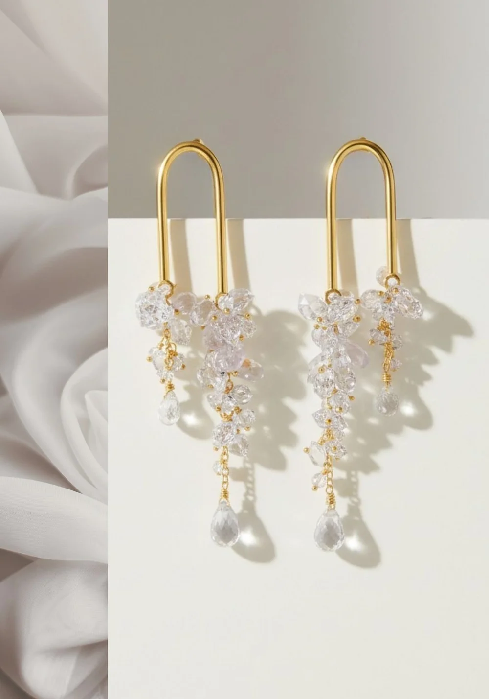 Gold arch earrings with cascading clusters of clear crystals and teardrop drops, on a white backdrop