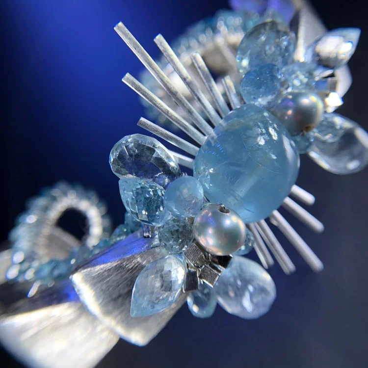 Macro of an Andrea Li aquamarine starburst cuff with brushed silver rays on deep blue, by Andrea Li