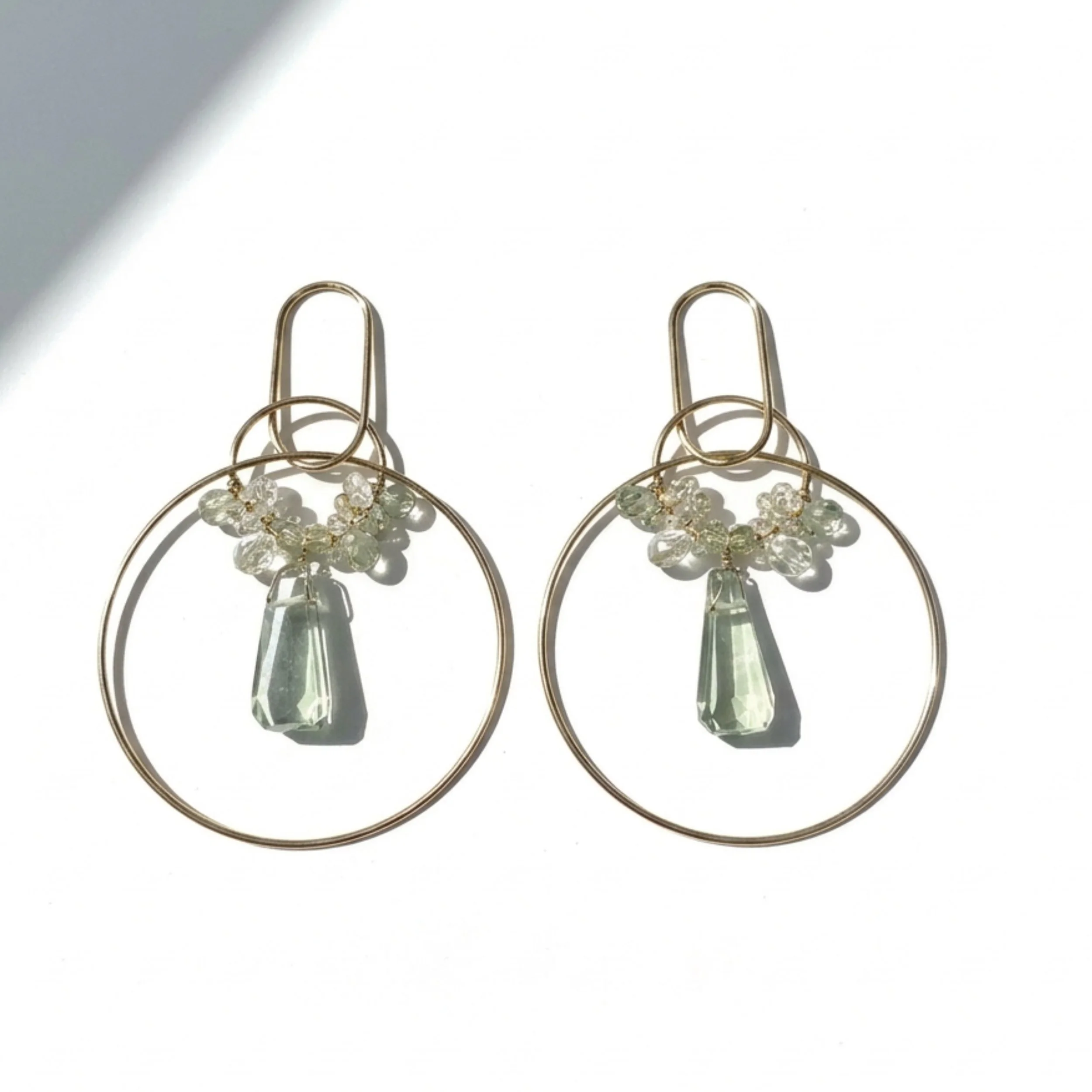 Gold hoop earrings with pale green gemstone drops and clustered pastel stones, displayed on a white background with soft shadows.