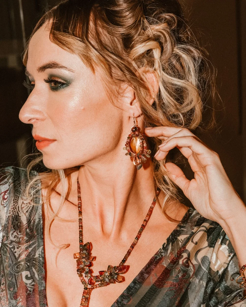 A model with curled blond hair touching her ear, wearing Andrea Li tourmaline drop earrings and a gemstone necklace, by Andrea Li