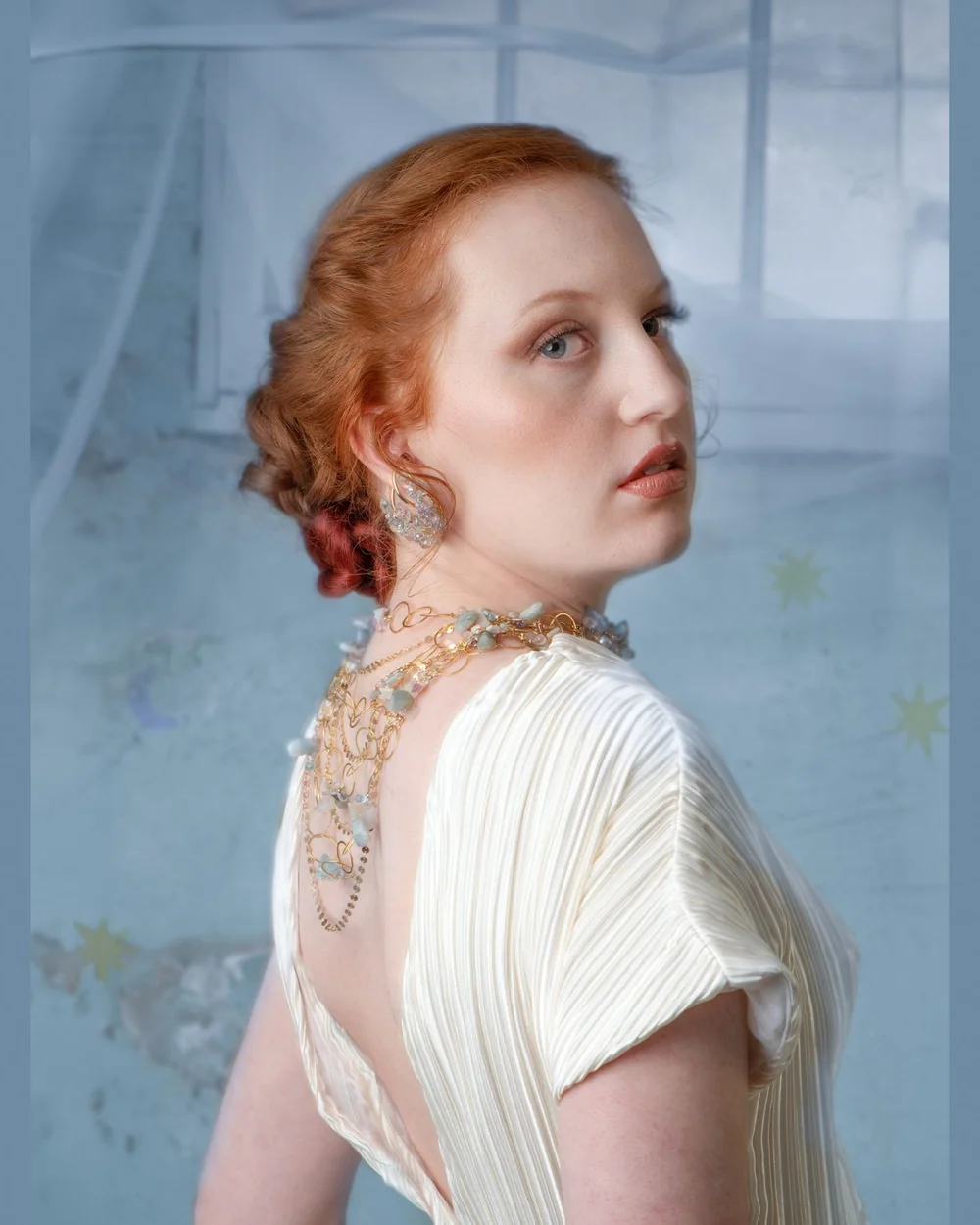 A red-haired model in a white pleated gown looking over her shoulder, wearing Andrea Li pastel gemstone earrings and a gemstone collar, by Andrea Li