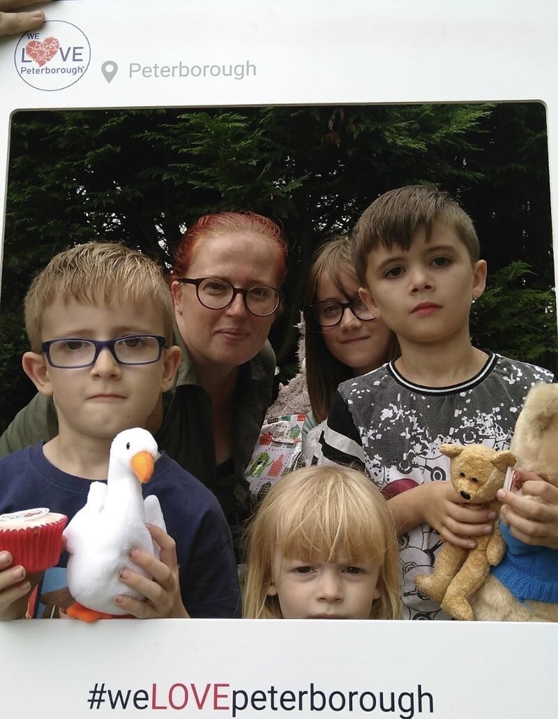 Image of a family looking into the camera. Four children, and a woman that looks like their mothers. One of the boys is holding a toy duck and a cupcake. the other boy is holding two teddy bears.