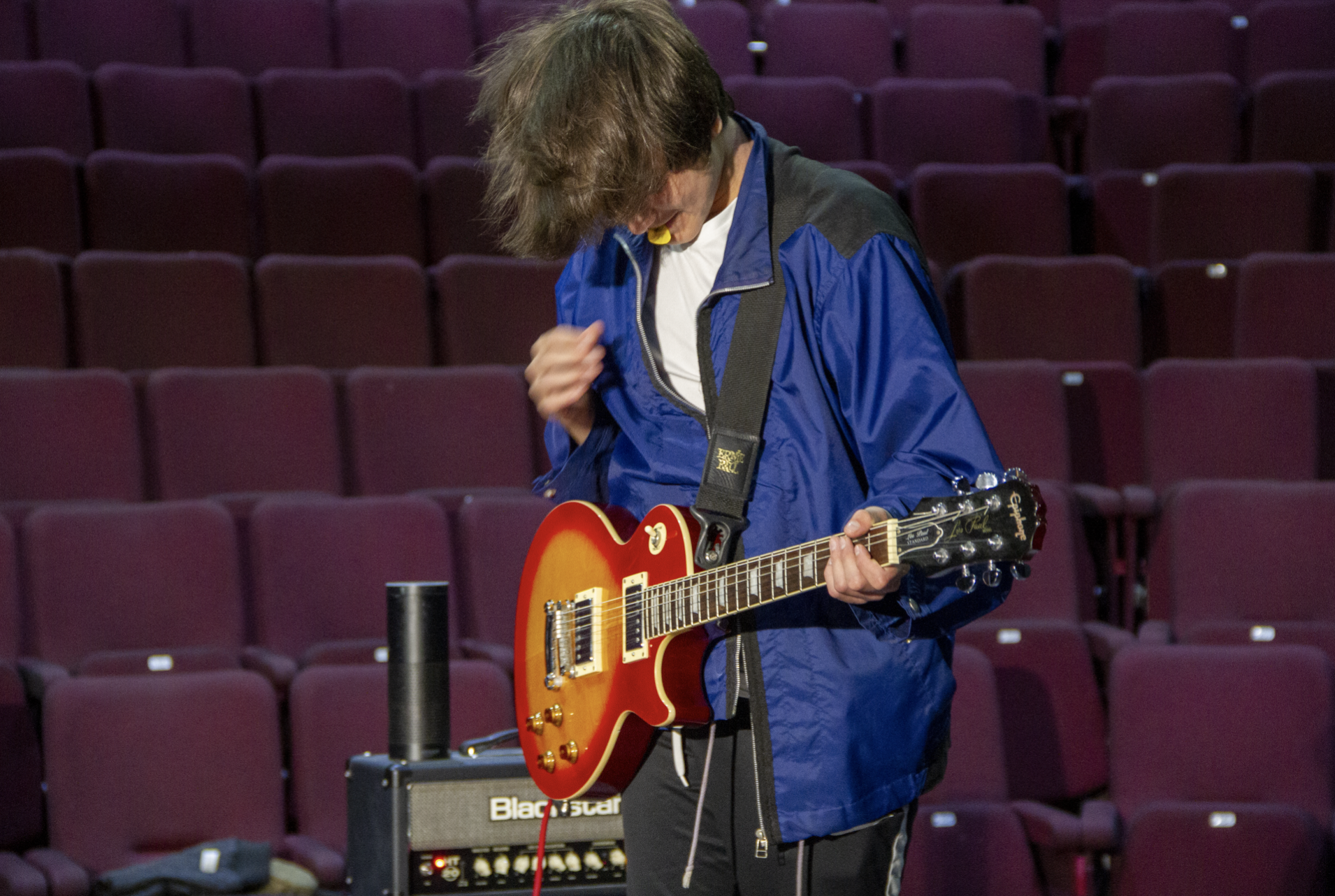 a young man with white skin and brown hair is passionately playing the guitar with a pick in his mouth.