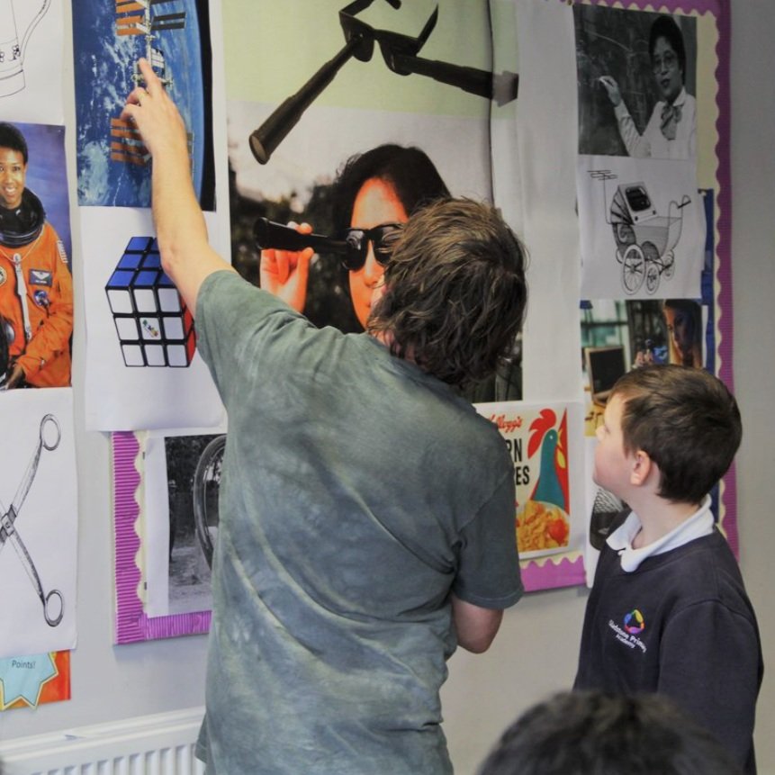  A man and a school child standing looking and pointing at a wall, which is covered in pictures 