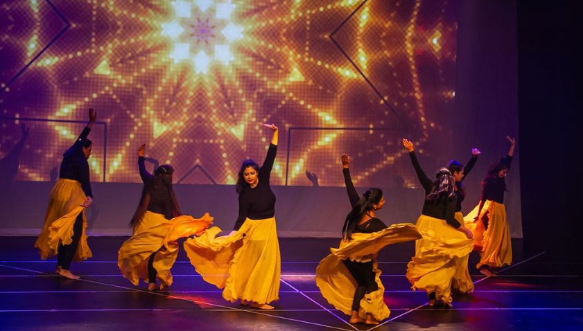  Seven women dancing onstage in costumes in front of a screen 
