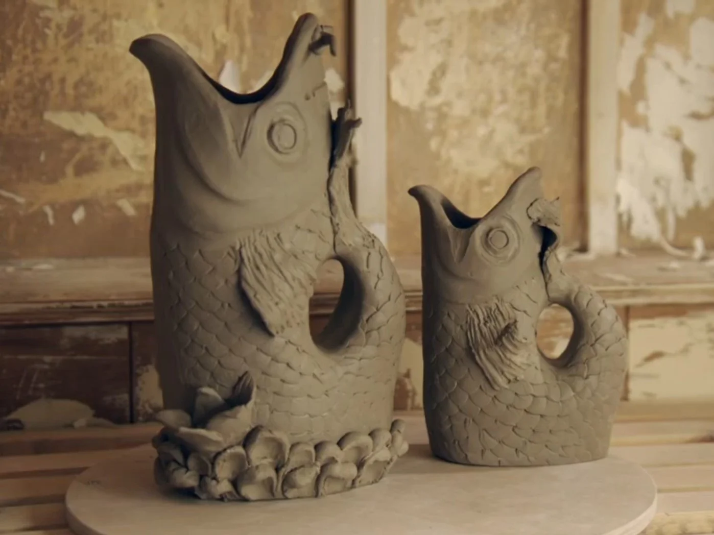 Two ceramic fish-shaped sculptures with open mouths and textured scales on display on a wooden surface.