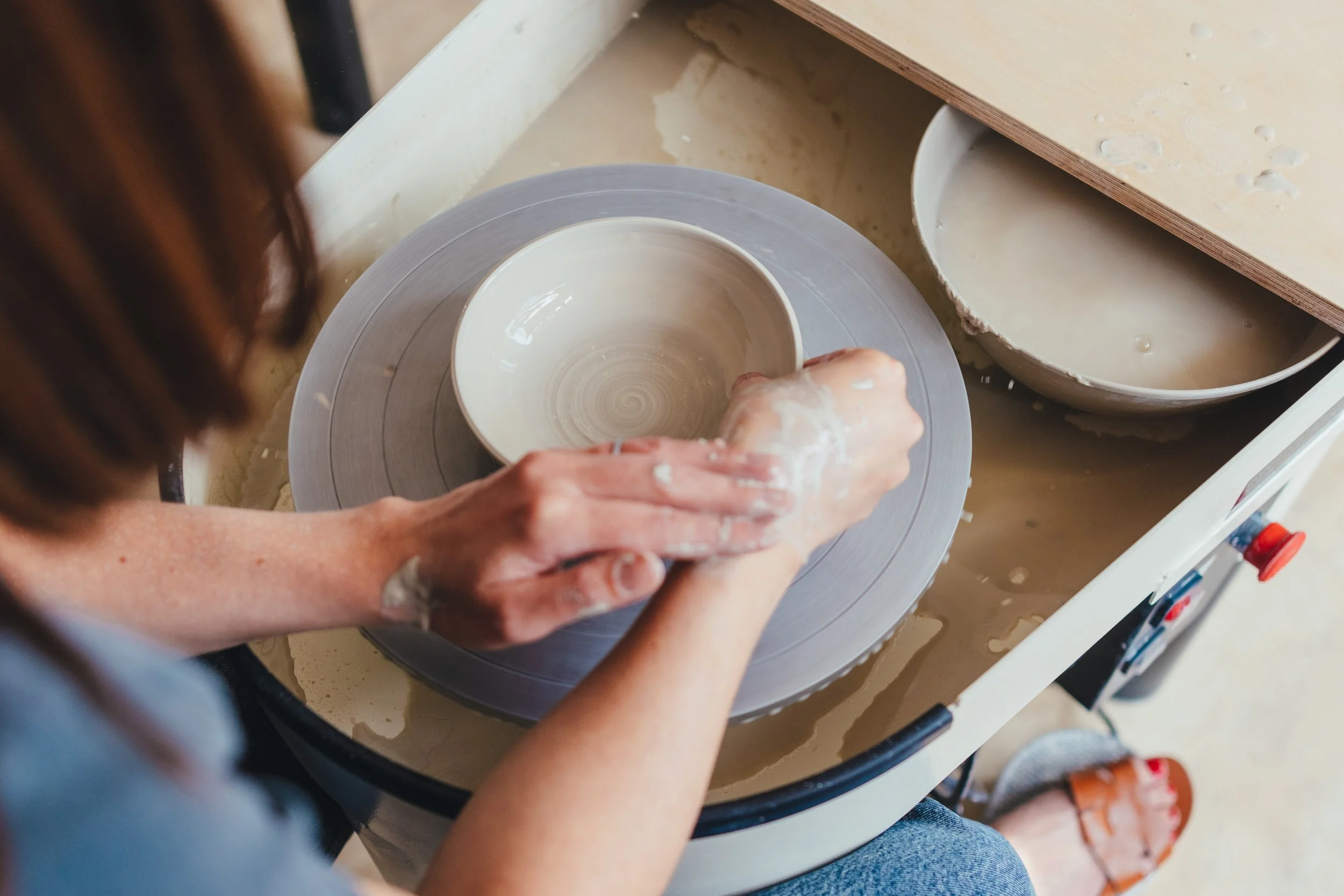 Person shaping a ceramic bowl on a pottery wheel in a pottery studio.