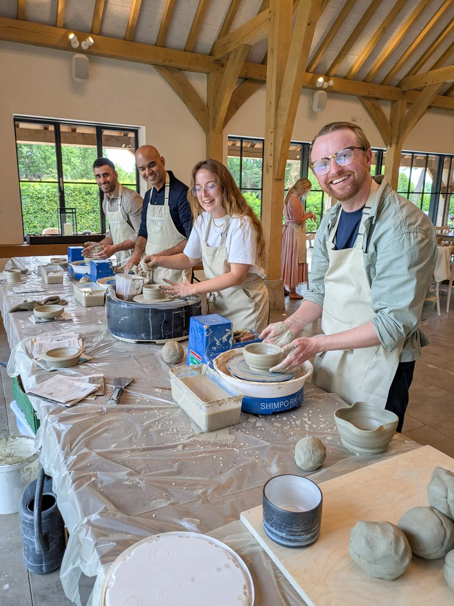 Group of five people smiling and working on pottery wheel in a Corporate pottery class, with clay and tools on the table.